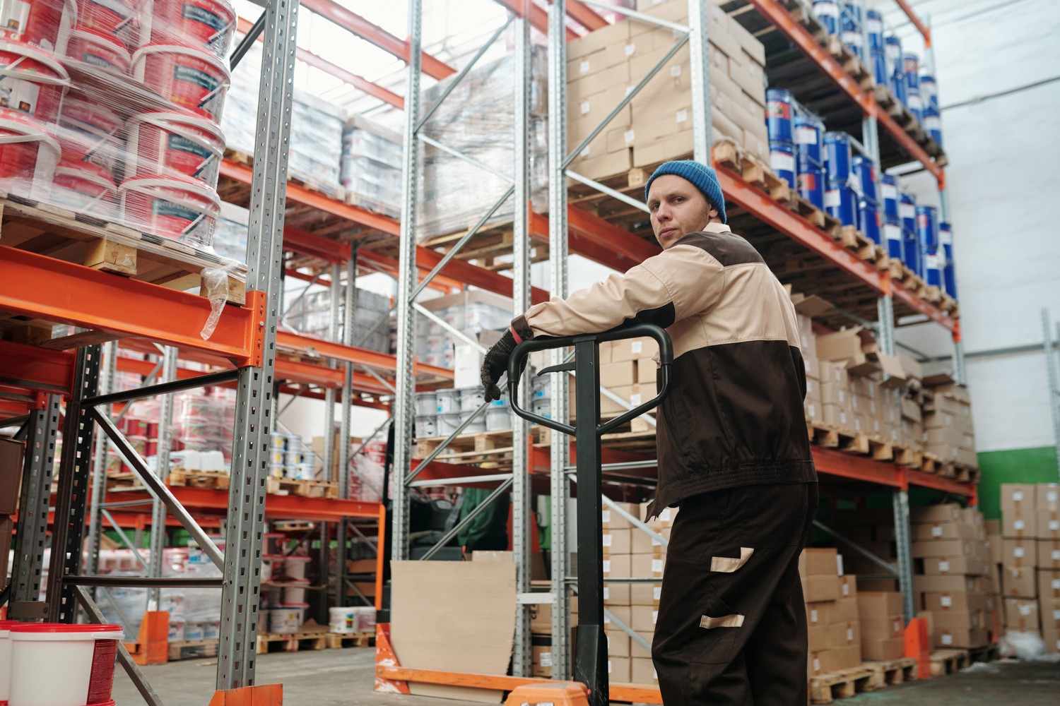 Warehouse worker handling a pallet jack beside packaged goods
